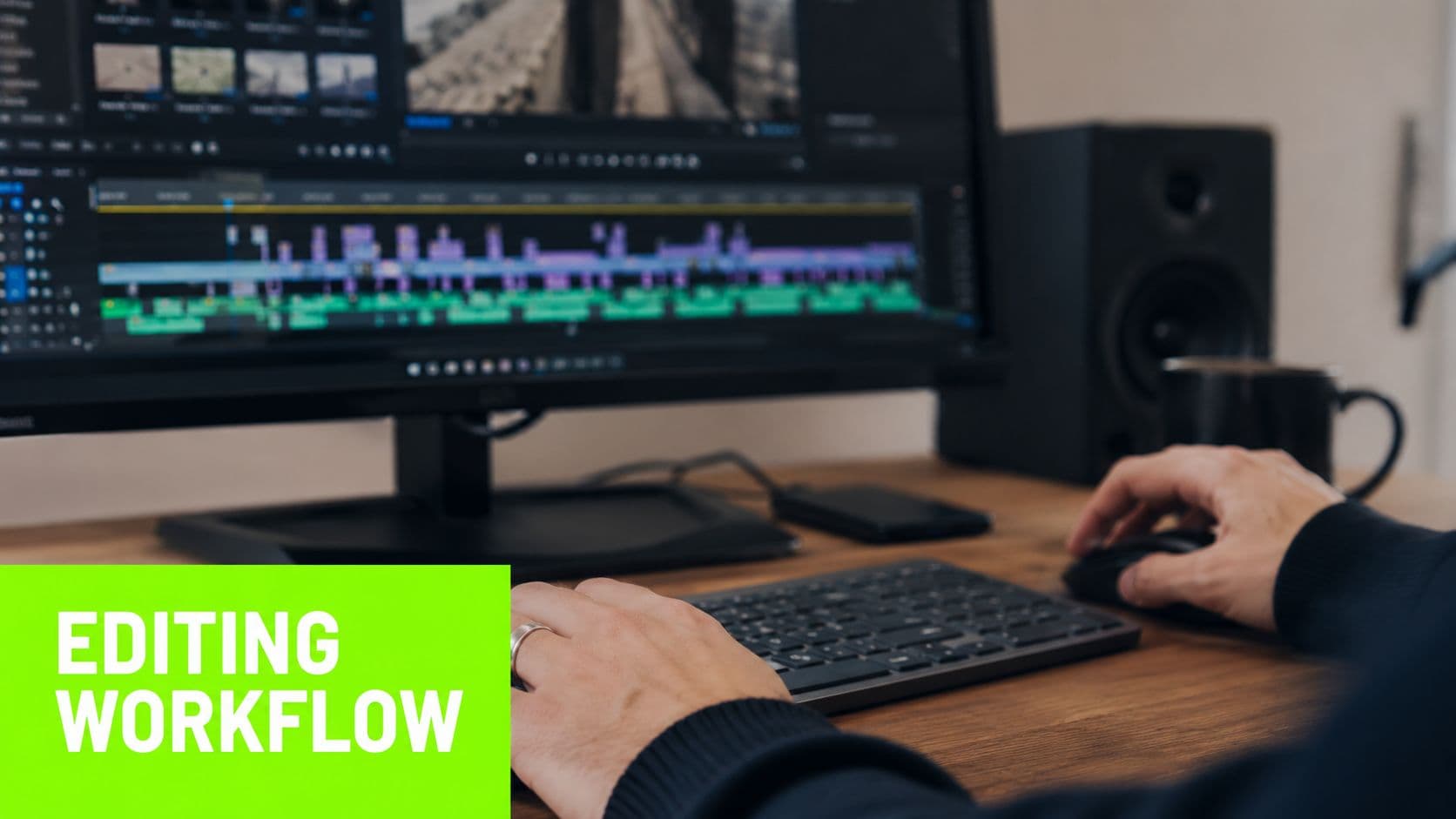 A person editing a video on a computer screen while working at a wooden desk setup.
